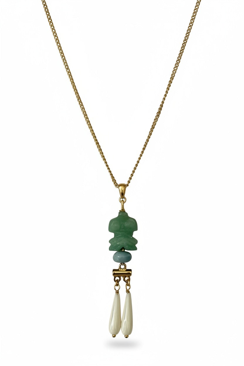 The SANDRINE FRANCE STUDIO - COMPANION COLE NECKLACE by SANDRINE FRANCE STUDIO features a gold chain with a green aventurine carved pendant, a small round bead, and two elongated white drops suspended from a gold connector, all beautifully displayed on a white background. This handcrafted accessory brings an elegant touch of sophistication to any ensemble.