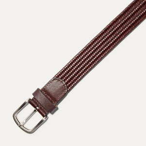 The WILL LEATHER GOODS - STRETCH BELT features a green, purple, and black braided design with full-grain leather accents by the silver buckle and tip, shown on a plain light background. Brand: WILL LEATHER GOODS.