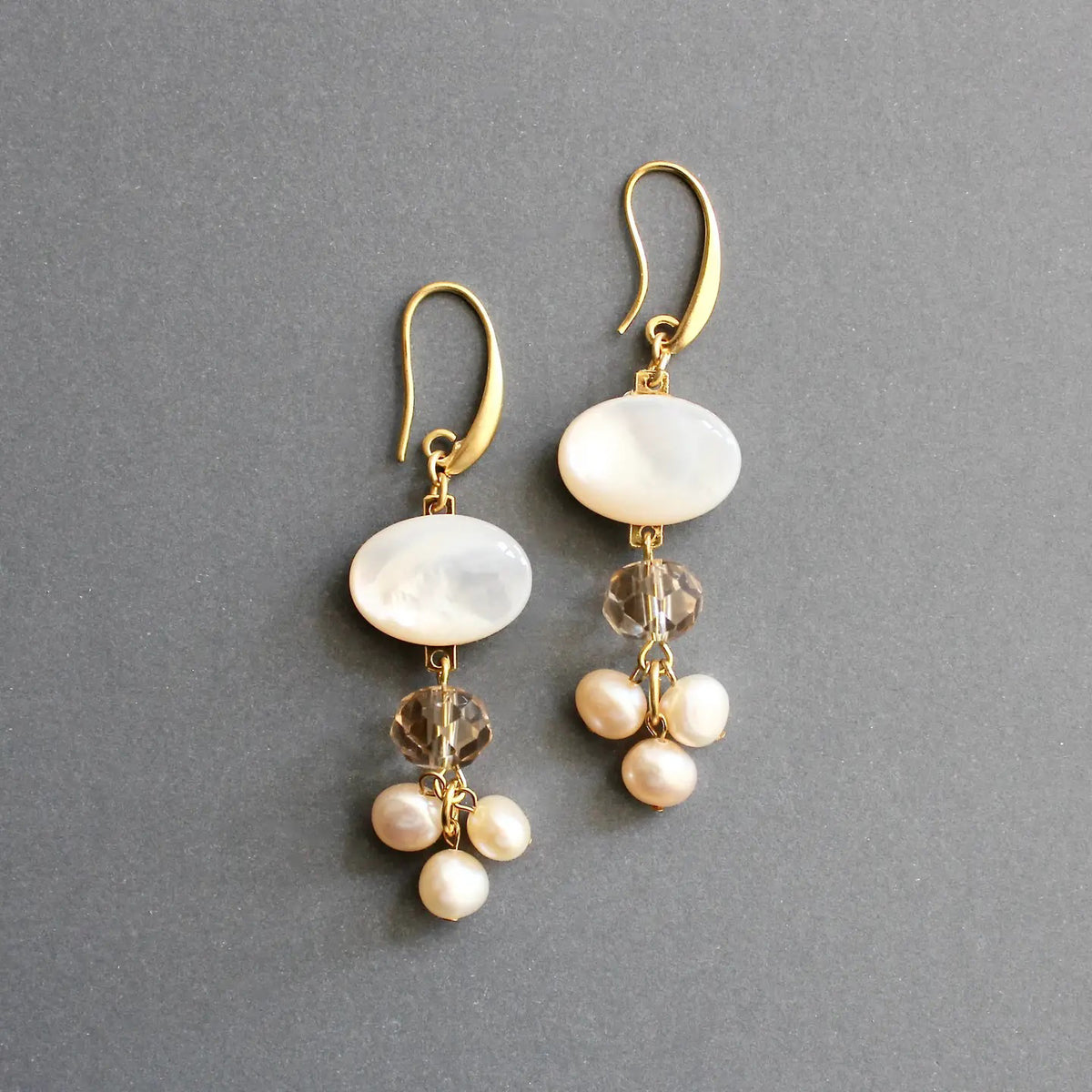 The DAVID AUBREY Mother of Pearl Cluster Earrings feature elegant 18k gold-plated hooks with a flat white oval bead, a faceted round bead, and clusters of pearl-like beads.