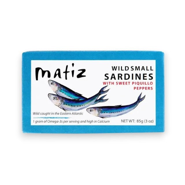 A rectangular package of MATIZ ESPANA Matiz - Sardinillas with Piquillo Peppers in Spanish Olive Oil. The blue package showcases an illustration of three sardines and includes details such as "Wild caught in the Eastern Atlantic," "1 gram of Omega-3's per serving," and "NET WT: 85g (3 oz).