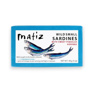 A rectangular package of MATIZ ESPANA Matiz - Sardinillas with Piquillo Peppers in Spanish Olive Oil. The blue package showcases an illustration of three sardines and includes details such as "Wild caught in the Eastern Atlantic," "1 gram of Omega-3's per serving," and "NET WT: 85g (3 oz).