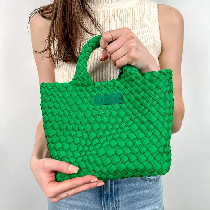 A woman with long brown hair, in a sleeveless cream knit top and blue jeans, holds a PARKER AND HYDE - MINI WOVEN TOTE BAG. The hand-woven tote by PARKER &amp; HYDE features a subtle checkered pattern with light blue accents.