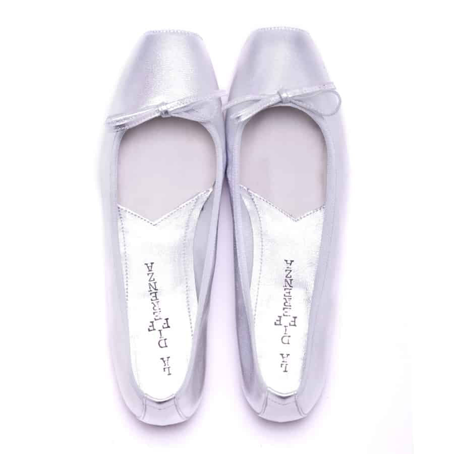 The MICHELE LOPRIORE - PALOMA ballet flat with a square toe, crafted from genuine silver leather, features a delicate bow on the front and a low-profile brown sole. Made in Italy, this elegant shoe is set against a plain white textured background.