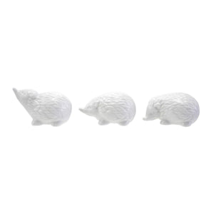 Six CREATIVE COOP WHITE STONEWARE HEDGEHOG figurines in different poses are arranged on and around three whitewashed cylindrical wooden pedestals, perfect for charming farmhouse decor. The background is plain white.