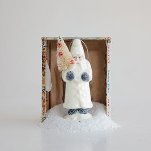 A white Creative Coop Vintage Belsnickel Ornament With Sisal Bottle Brush holds a miniature sisal tree decorated with small red ornaments.