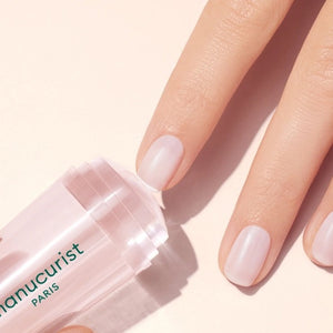 A hand with a light pink French manicure rests beside the MANUCURIST - MANI STAMPER by MANUCURIST INC on a pale background.