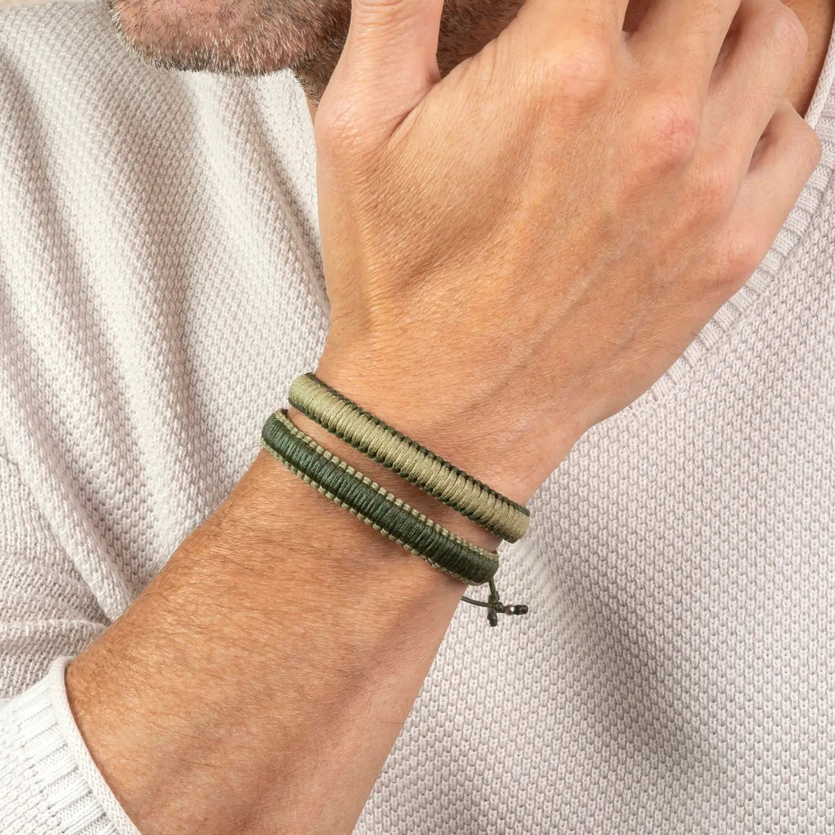A close-up of a person’s hand resting on their chin, wearing two MAKARLA MEN'S REVERSIBLE SURFER BRACELETS in light blue and navy, paired with a light knit sweater.
