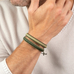 A close-up of a person’s hand resting on their chin, wearing two MAKARLA MEN'S REVERSIBLE SURFER BRACELETS in light blue and navy, paired with a light knit sweater.
