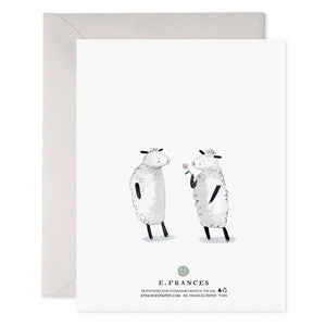 E. FRANCES - THANK EWE CARD by E. FRANCES PAPER features a watercolor design with two cartoon sheep, one holding a pink flower behind its back. The cheerful words "THANK EWE" appear above them in playful lettering. A gray envelope is partially visible behind the card. Proudly made in the USA.