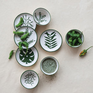 CREATIVE COOP's HAND-PAINTED STONEWARE BOWLS WITH BOTANICAL DESIGN, some holding green peppers or grains, are arranged on a light beige surface—each bowl highlights its unique handcrafted artistry.