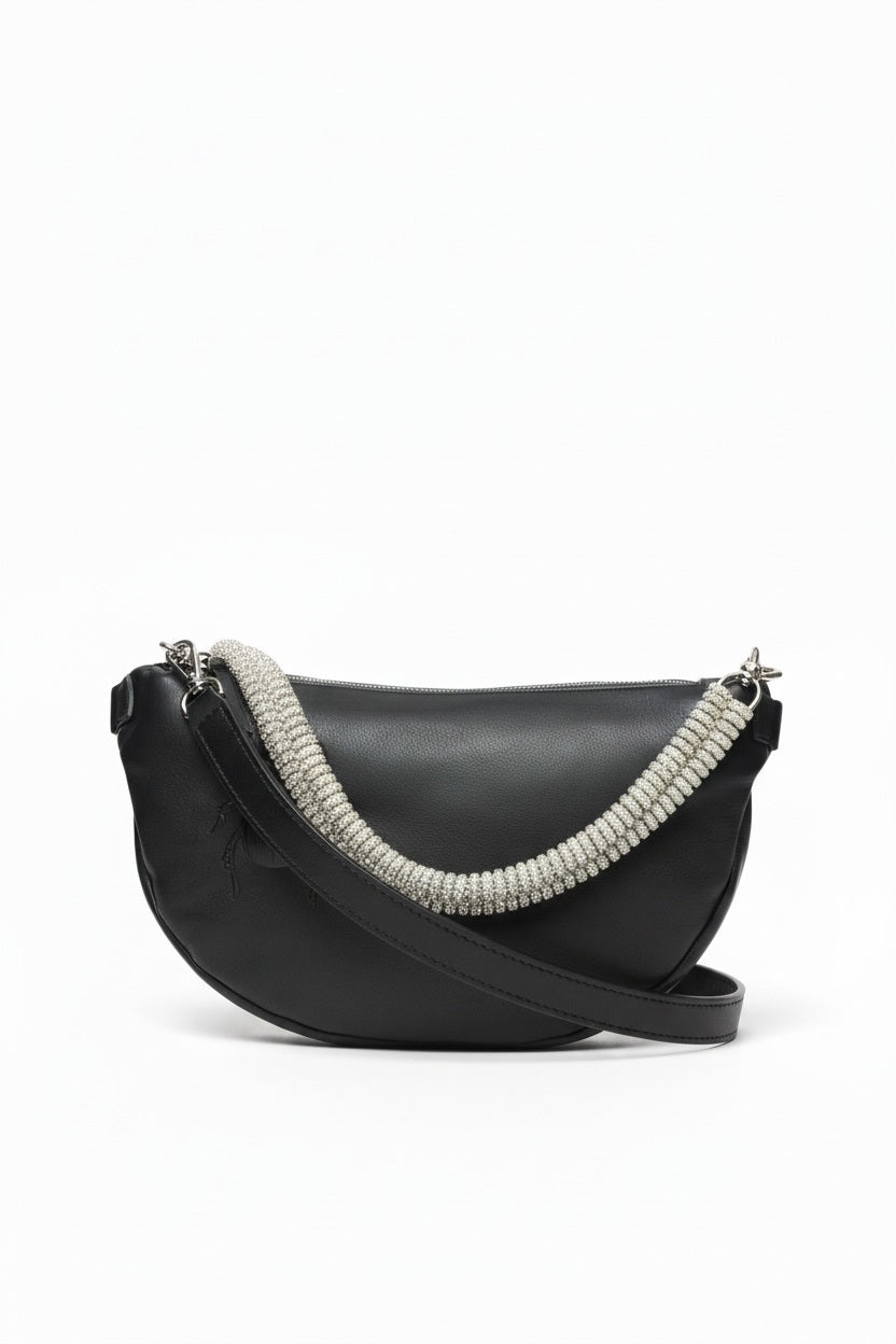 The GANRIELE FRANTZEN - SCARAB LEATHER XL BELT BAG IN BLACK WITH EXTRA CRYSTAL STRAP by GABRIELE FRANTZEN is a black leather, crescent-shaped crossbody bag featuring a long black strap and an extra decorative crystal handle, displayed against a plain white background.
