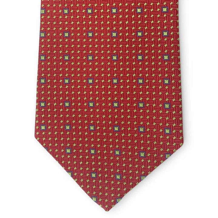 A close-up of the BIRD DOG BAY PETER-BLAIR - BESPOKE FINE SQUARES SILK TIE IN RED, a handmade silk tie featuring a red base with a geometric grid of small yellow and blue squares, finishing in a pointed tip.