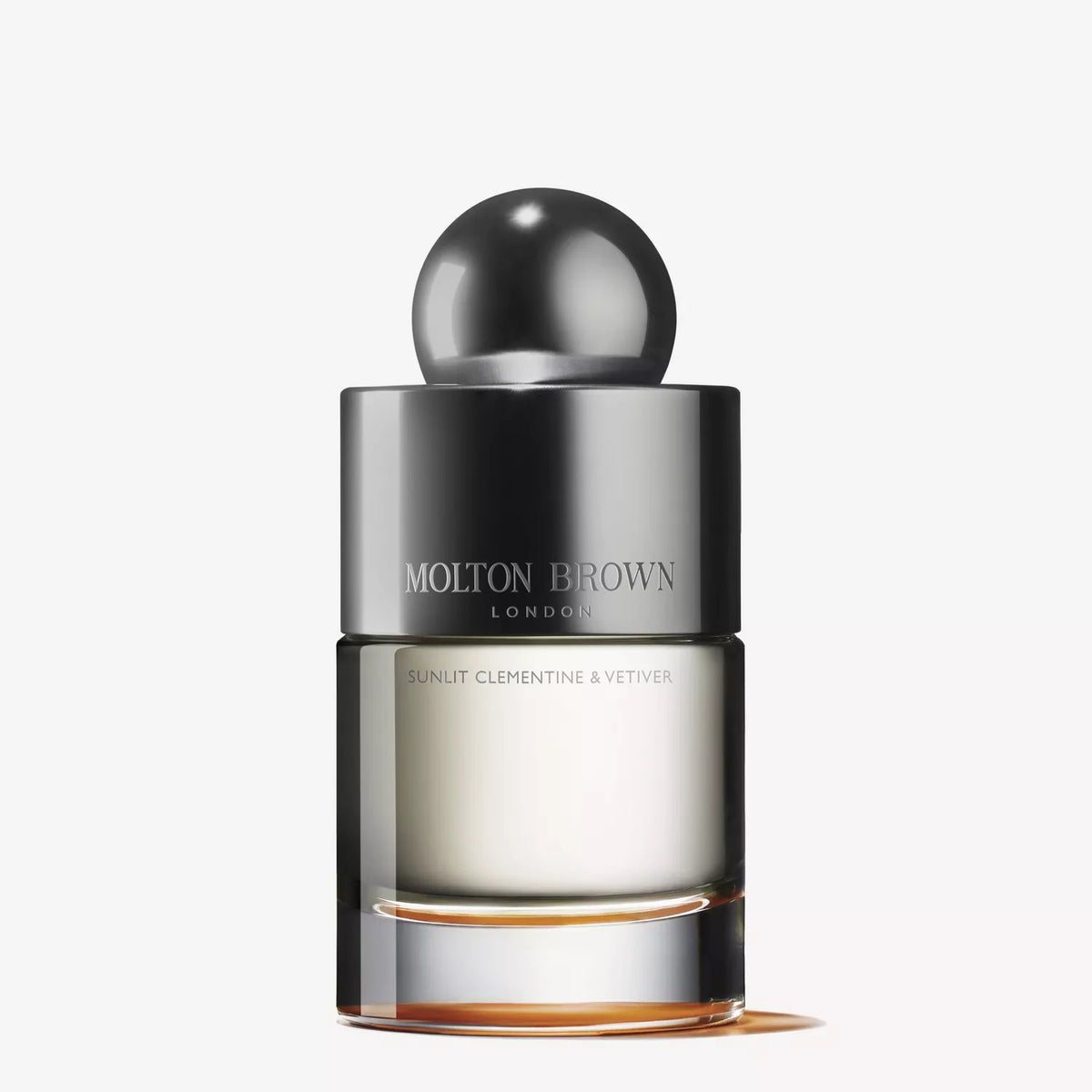 A clear glass bottle of MOLTON BROWN - SUNLIT CLEMENTINE &amp; VETIVER EAU DE TOILETTE with a metallic cap and minimalist design is displayed against a plain white background.