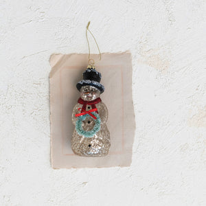 The CREATIVE COOP MERCURY GLASS SNOWMAN ORNAMENT features a vintage look with a black top hat, red scarf, green wreath, gold string hanger, and an antique-style finish.