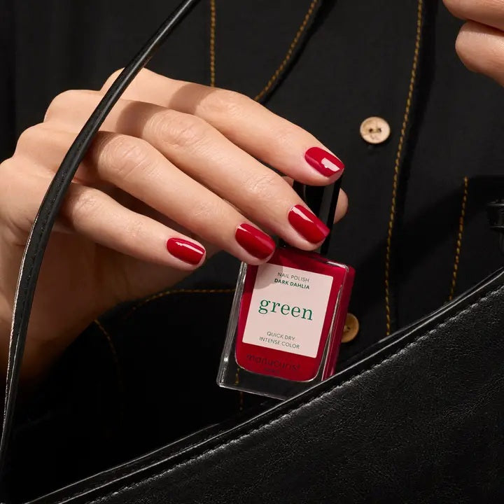 A hand with neatly manicured nails painted in MANUCURIST - GREEN™ NAIL POLISH IN DARK DAHLIA by MANUCURIST INC rests on a light pink, long-sleeve garment. The lighting highlights the glossy finish of the nail polish.
