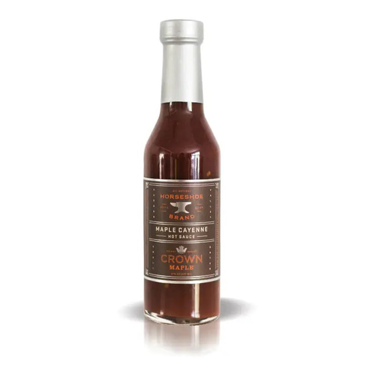 A glass bottle of CROWN MAPLE - HORSESHOE HOTSAUCE by Crown Maple. Filled with a red-brown sauce, it sports a silver cap and a brown label accented with white and orange text, detailing the blend&#39;s robust crown maple and cayenne pepper flavor, along with the brand’s logo and product specifics.