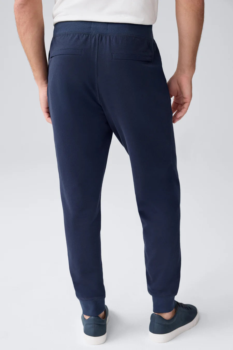 A person wears MACK WELDON ACE Relaxed Fit Sweatpants in True Navy - Bird’s Eye, styled with pockets and matching navy sneakers, against a plain light gray background. Only the lower body is visible.