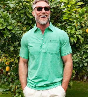 A person wears the CRIQUET Top-Shelf Players Shirt in Golf Green Microstripe with white buttons and a front pocket displaying a small embroidered logo; their face is partially out of frame.