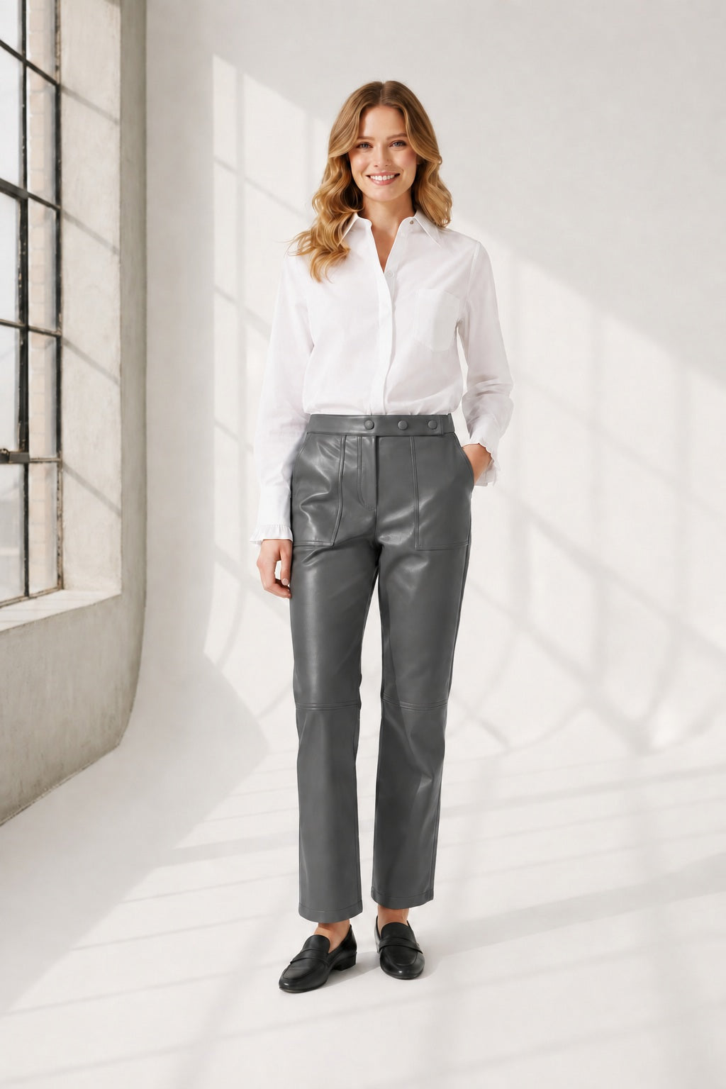 A person wearing high-waisted brown leather pants, a white long-sleeve shirt, and brown heeled ankle boots, standing against a plain light background. The person's face is not visible.