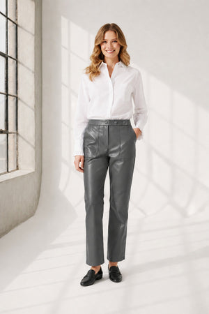 A person wearing high-waisted brown leather pants, a white long-sleeve shirt, and brown heeled ankle boots, standing against a plain light background. The person's face is not visible.