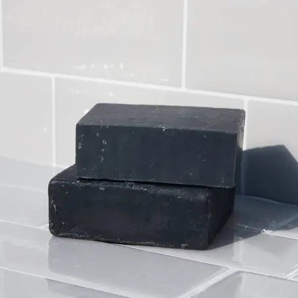 The KITSCH - CHARCOAL DETOXIFYING BODY WASH BAR, a black square solid soap on a matching box, is gentle, vegan, and all-natural. Detoxify pores and refresh your skin with this 4 oz. (113g) zero-waste treat while embracing an eco-friendly lifestyle.