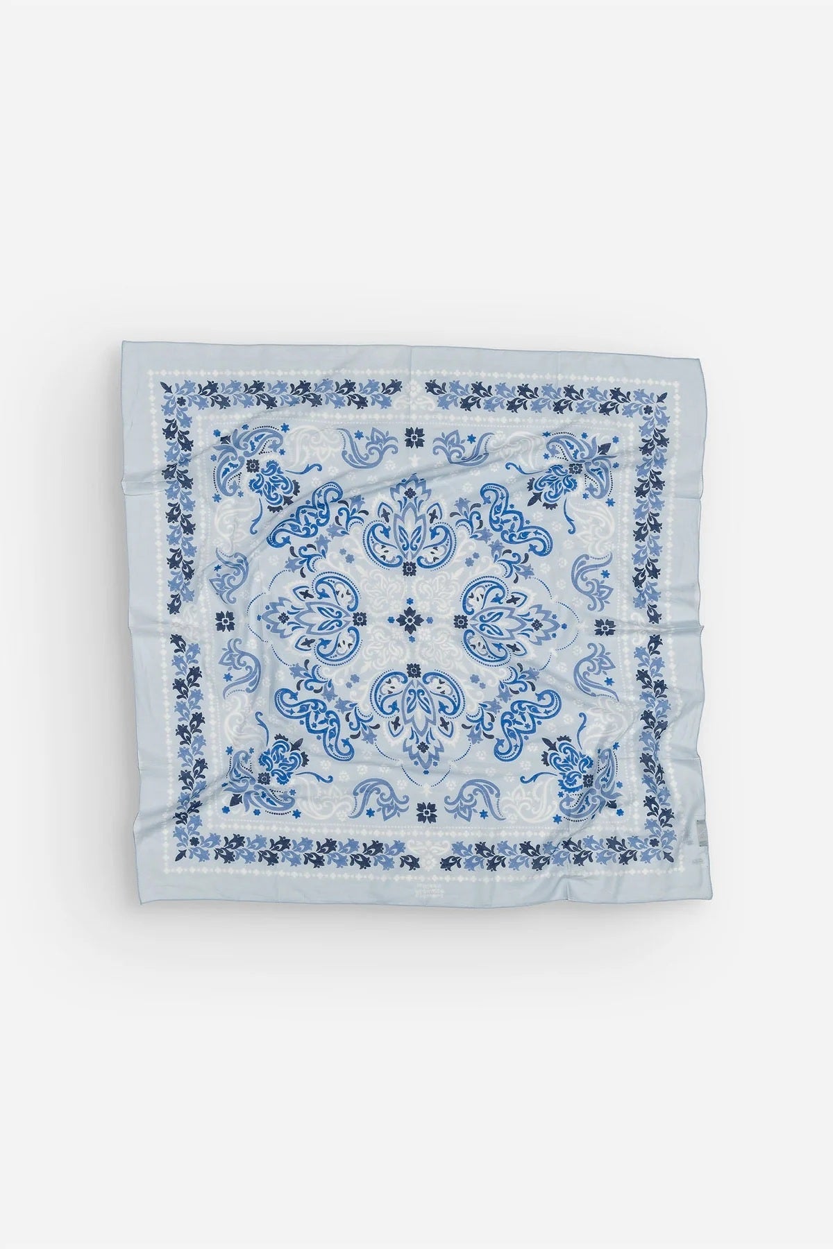 The MAISON LECOMTE - DINARD BANDANA SCARF IN COTTON VOILE by MAISON LECOMTE FLAMENT is a square, light blue cotton voile bandana adorned with an intricate paisley and floral pattern in shades of dark and light blue, elegantly displayed flat on a white background—an ideal accessory for any occasion.