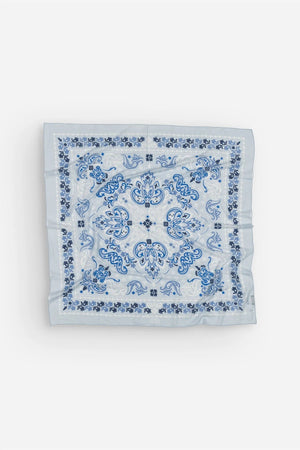 The MAISON LECOMTE - DINARD BANDANA SCARF IN COTTON VOILE by MAISON LECOMTE FLAMENT is a square, light blue cotton voile bandana adorned with an intricate paisley and floral pattern in shades of dark and light blue, elegantly displayed flat on a white background—an ideal accessory for any occasion.