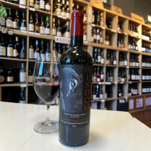 A bottle of 2018 B. WISE VINEYARDS ‘WISDOM’ CABERNET SAUVIGNON with a red foil capsule and a black label featuring an image of a Buddha statue and the word “WISDOM” in red vertical text.