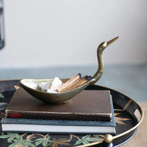The CREATIVE COOP BIRD SHAPED BOWL IN ANTIQUE BRASS FINISH features a cast aluminum body with an elongated neck and beak, resembling a crane or heron for a stunning decorative accent.