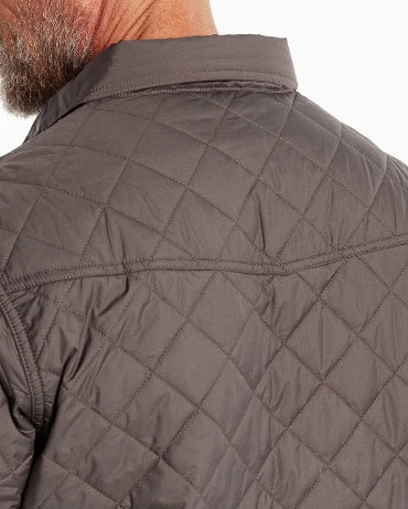 A smiling man with gray hair and a beard wears the CRIQUET - QUILTED SHACKET IN CHARCOAL by CRIQUET over a light shirt and tan pants, standing against a white background.