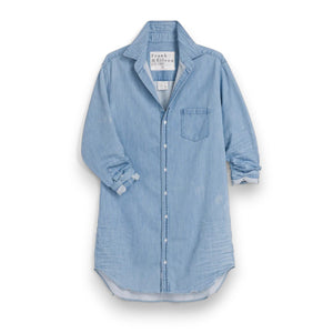 A woman smiles outdoors in the FRANK & EILEEN Mary Classic Shirtdress in Famous Denim Classic Wash, standing amid garden greenery and patio furniture.