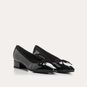 The REQINS FETICHE heeled ballerina shoe features black patent leather, a rounded toe, small bow detail, and a block heel, shown on a plain white background.