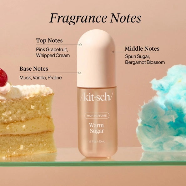 A bottle of KITSCH - HAIR PERFUME MIST IN WARM SUGAR stands between a slice of cake and blue cotton candy, with labeled fragrance notes: pink grapefruit, whipped cream, spun sugar, bergamot blossom, musk, vanilla, and praline. This odor-eliminating formula from KITSCH ensures your hair smells irresistibly sweet and fresh all day.