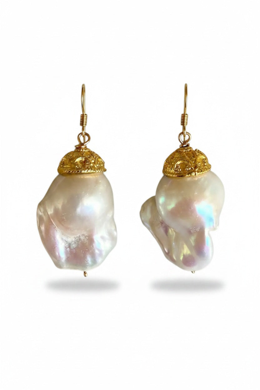 BITTERSWEET DESIGNS - CAPPED IVORY BAROQUE PEARL EARRINGS: Elegant, iridescent ivory baroque pearls with ornate gold caps and hoops from BITTERSWEET DESIGNS are displayed on a light gray textured surface.
