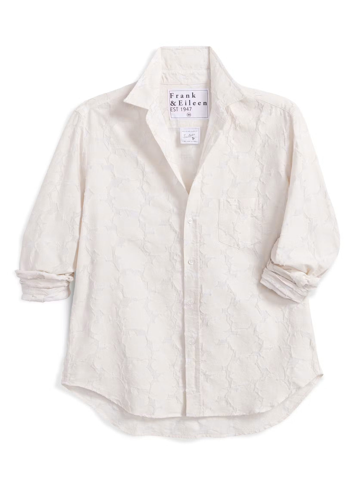 Introducing the FRANK & EILEEN - EILEEN Relaxed Button Up in Italian Cotton Textured Natural Flowers: a long-sleeve, button-up white shirt with a subtle floral texture, rolled cuffs, and a pointed collar. Designed for a relaxed fit, this shirt is crafted from premium Italian cotton and features thoughtfully placed buttons to flatter the bust for an effortlessly stylish silhouette. The signature label inside reads “FRANK & EILEEN EST 1947.”.