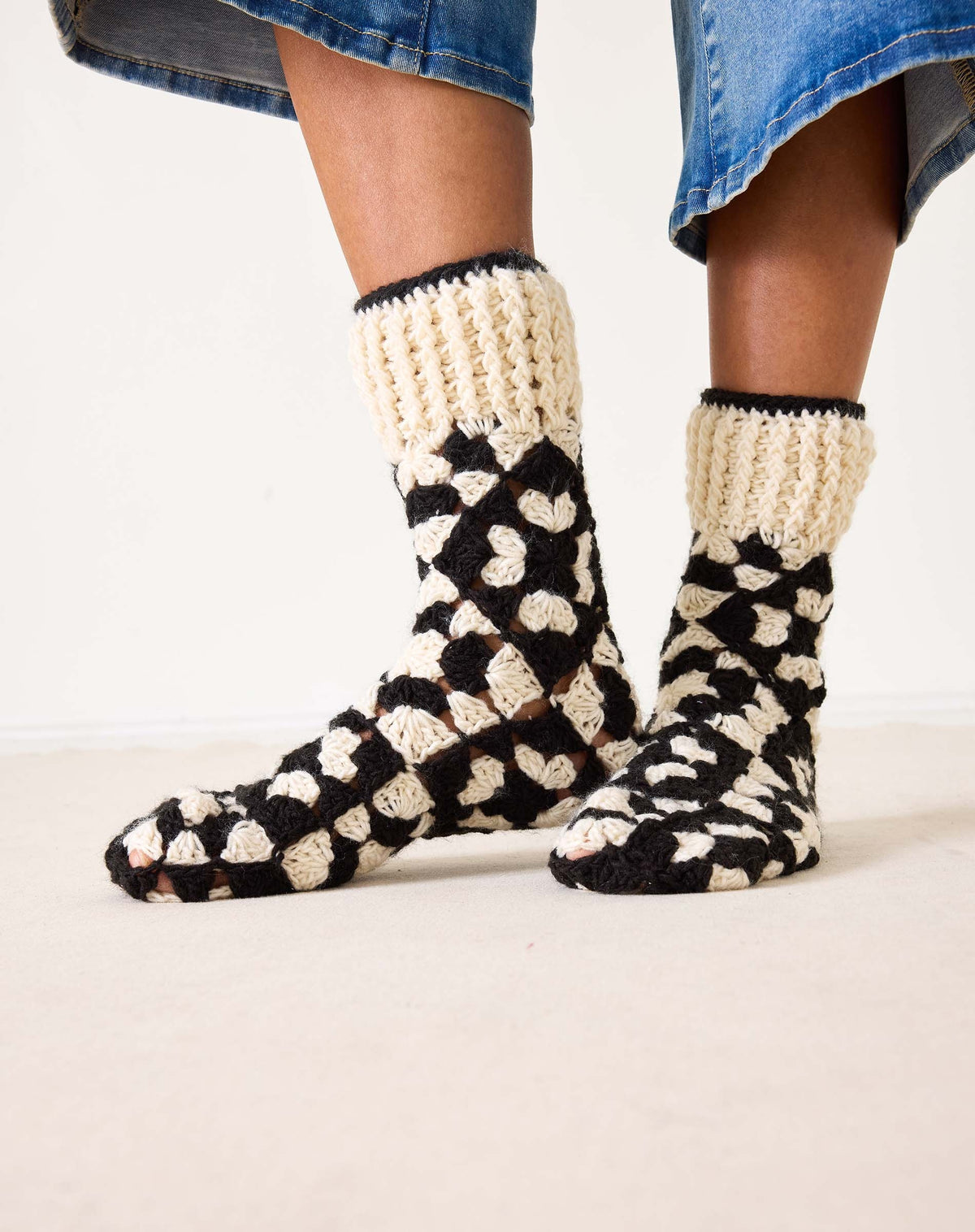 Introducing the MERSEA - LA PAZ CROCHET SLIPPER SOCKS by MERSEA: These hand-crocheted slipper socks feature a striking black and cream geometric design. The toes, heels, and cuffs are crafted in a solid cream shade, while the body showcases alternating black and cream sections—resulting in cozy socks you'll love to slip on.