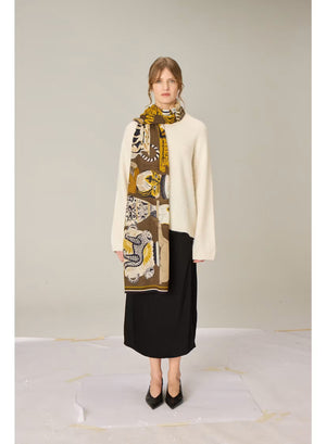The INOUI EDITIONS - COLLECTIONNEUR Wool Scarf with Cats in Khaki by INOUI is a rectangular accessory crafted in India from 100% wool. It features an artistic collage-like pattern of illustrated cats and circular motifs in shades of gold, white, black, and gray set against a dark khaki background. Measuring 70 x 190 cm, this striking scarf adds both warmth and a touch of artistry to any ensemble.