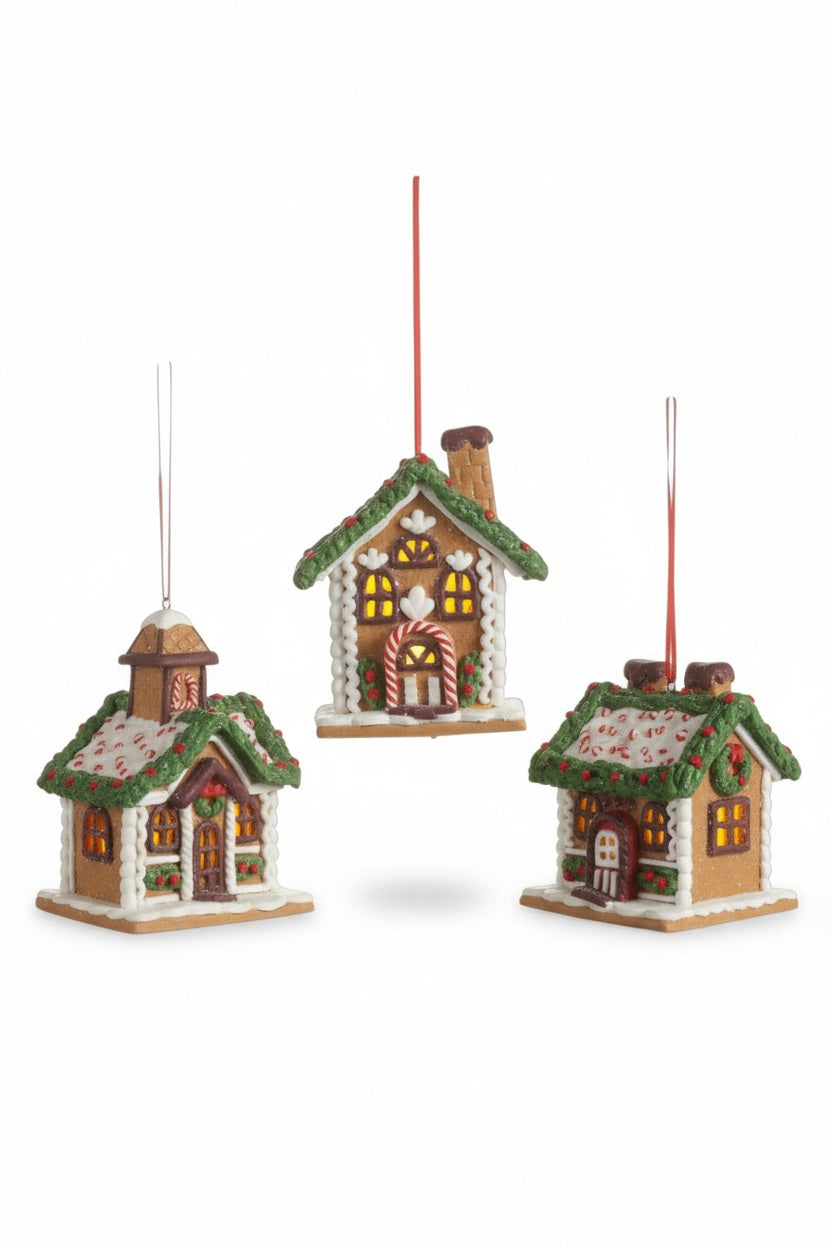 Three RAZ IMPORTS CHOCOLATE LIGHTED GINGERBREAD HOUSE ORNAMENTS in assorted styles with white icing trim, green roofs, and glowing windows, each hanging by a red string.