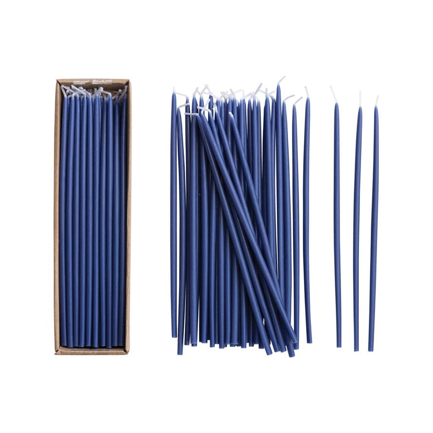 The CREATIVE COOP UNSCENTED THIN TAPER CANDLES IN NAVY are displayed in an open box containing 36 neatly arranged candles, with several matching navy candles laid side by side on a white background.