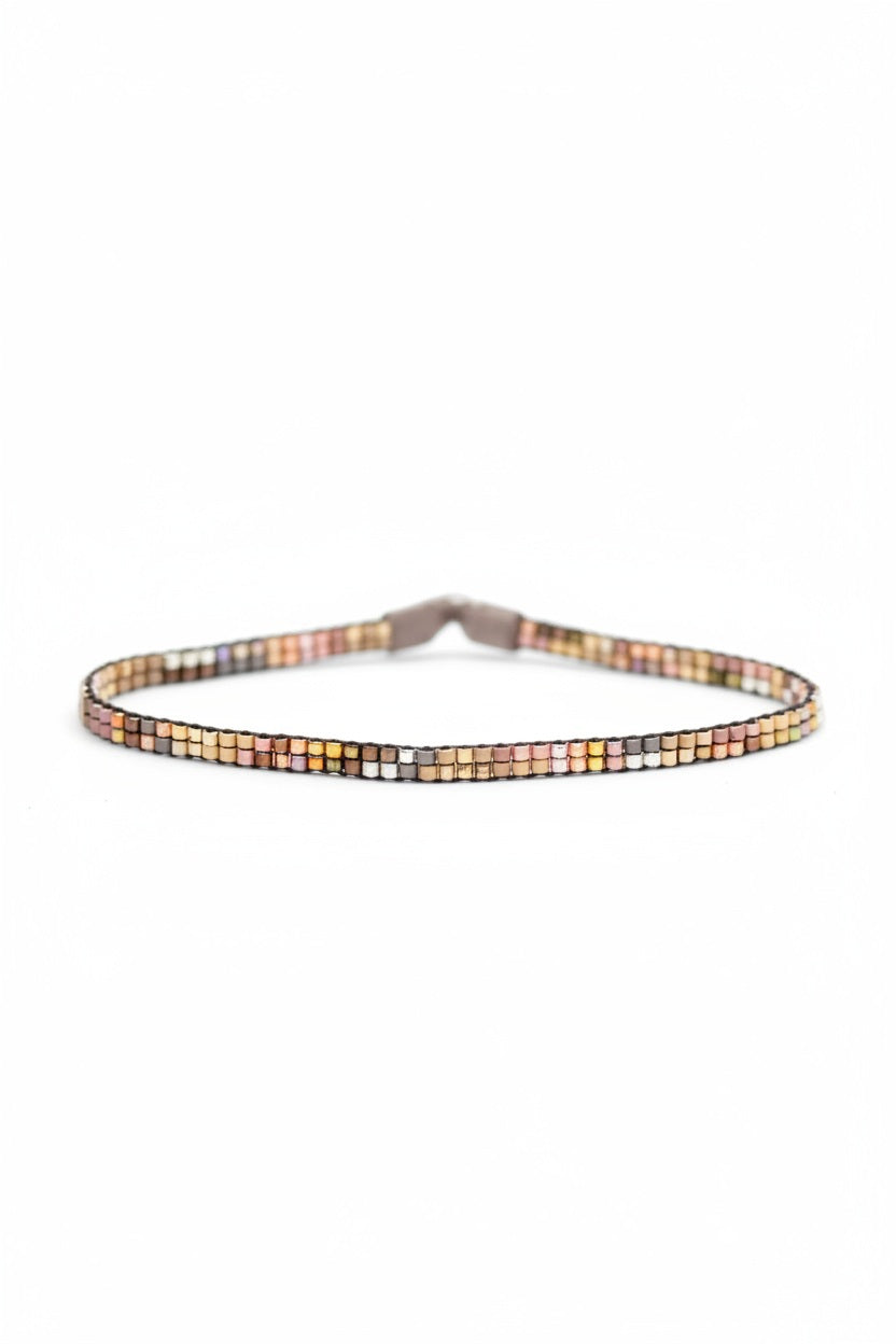 The JULIE ROFMAN - MINI BRACELET by JULIE ROFMAN JEWELRY is a vibrant handwoven piece adorned with small, square beads in various shades of pink, red, and white. It is displayed against a white background and includes a straightforward sterling silver clasp for convenient fastening.