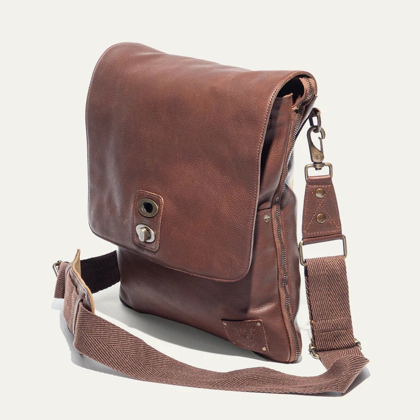 The WILL LEATHER GOODS - OTTO CROSSBODY BAG IN COGNAC, a full-grain leather bag with plaid lining, is shown open from above holding a camera, book, and wallet.