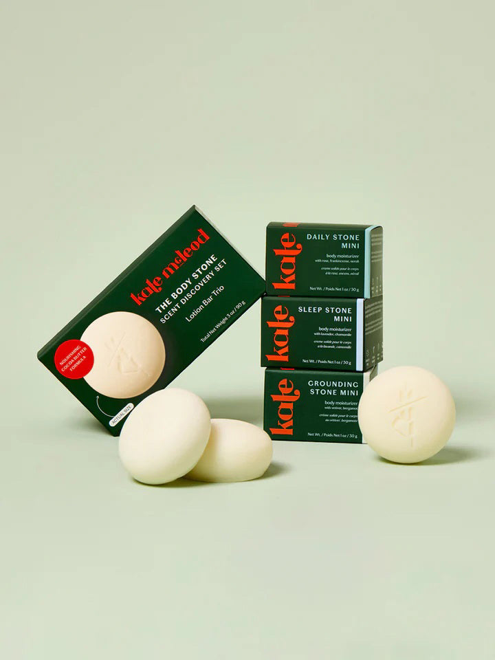 The KATE MCLEOD - THE ESSENTIAL COLLECTION MINI SAMPLER SET, featuring "The Body Stone," "Sleep Stone," and "Grounding Stone," is displayed against a light green background with three round stones in front and the brand box labeled behind.