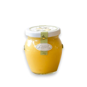 A jar of zesty BELLA CUCINA - LEMON CREAM with a white lid, is beautifully adorned with a green ribbon featuring a small lemon graphic. The label on the front, in elegant lettering, reads "BELLA CUCINA - LEMON CREAM," and the jar is set against a simple white background.