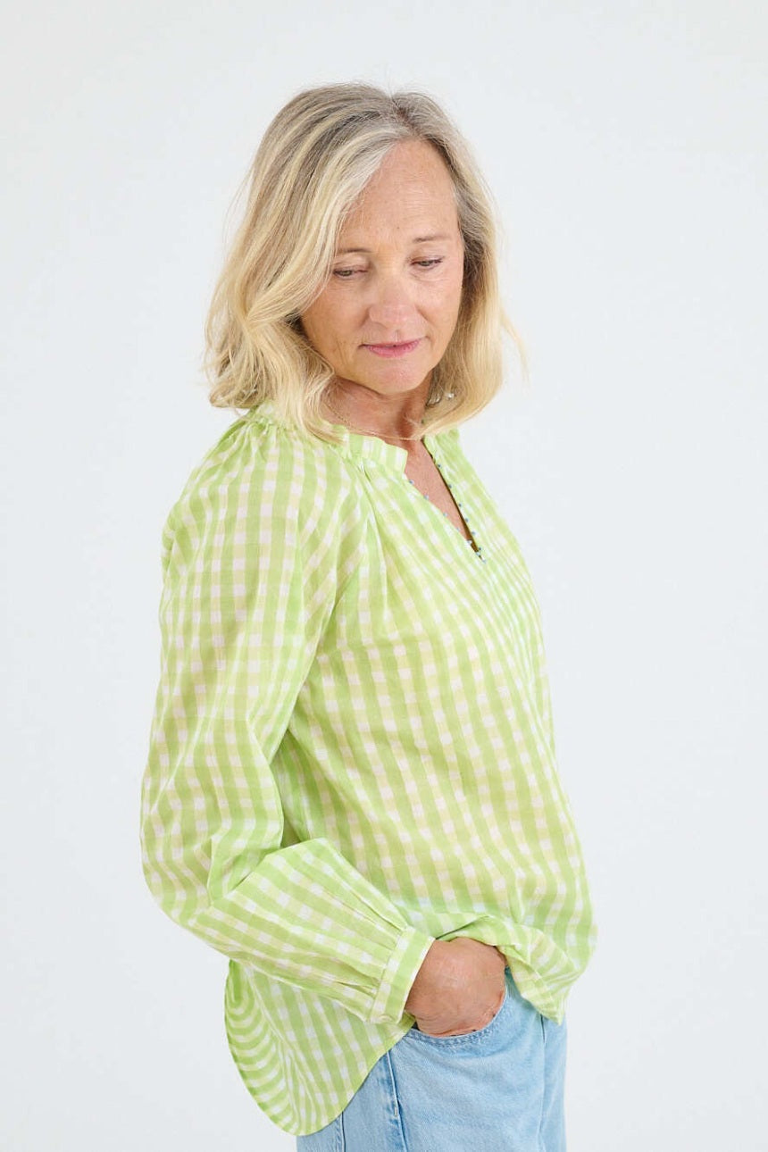 A person with shoulder-length blonde hair, seen from behind, wears the STORIATIPIC IRIS GINGHAM BLOUSE IN GREEN—featuring a light green and white check pattern and embroidered collar—with light blue jeans against a plain white background.