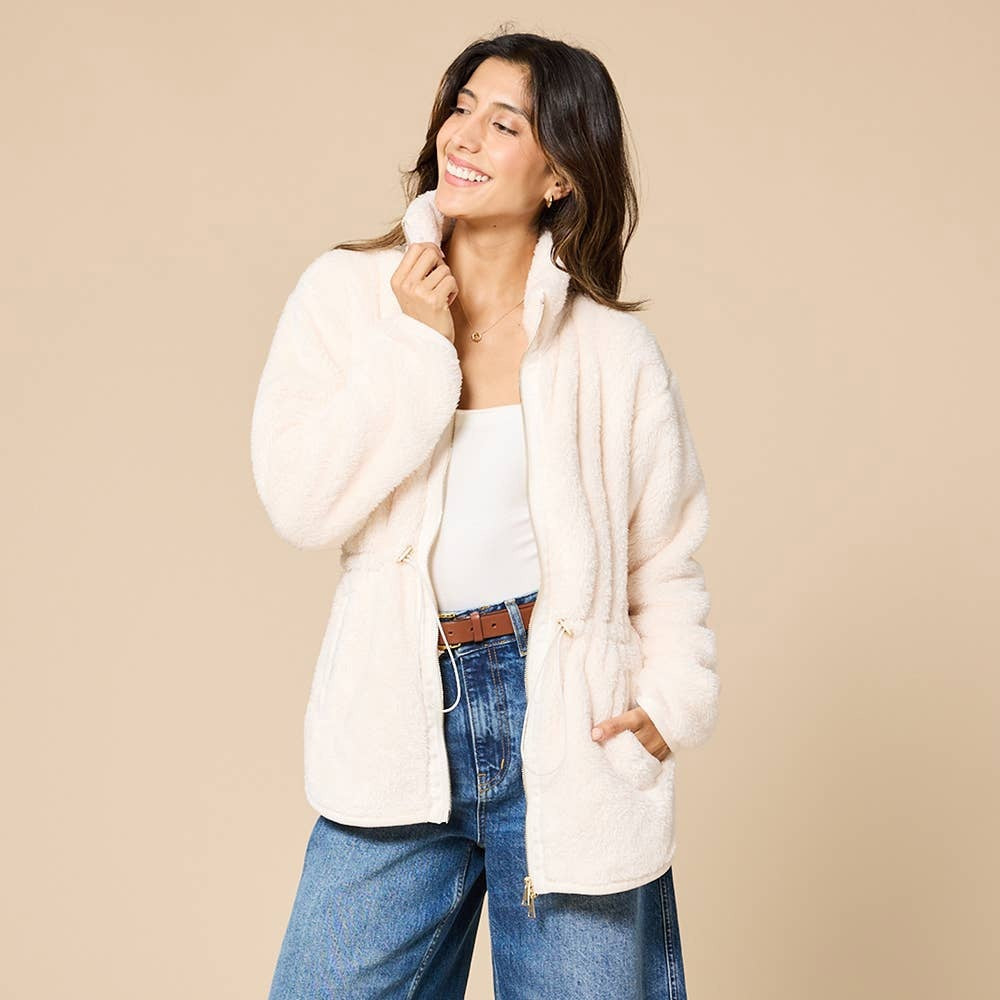 A woman wearing a cream SOFTIES - DREAMPLUSH DOUBLE ZIP JACKET / TUNIC with a cinched waist, paired with wide-leg denim culottes for cozy velvety softness.
