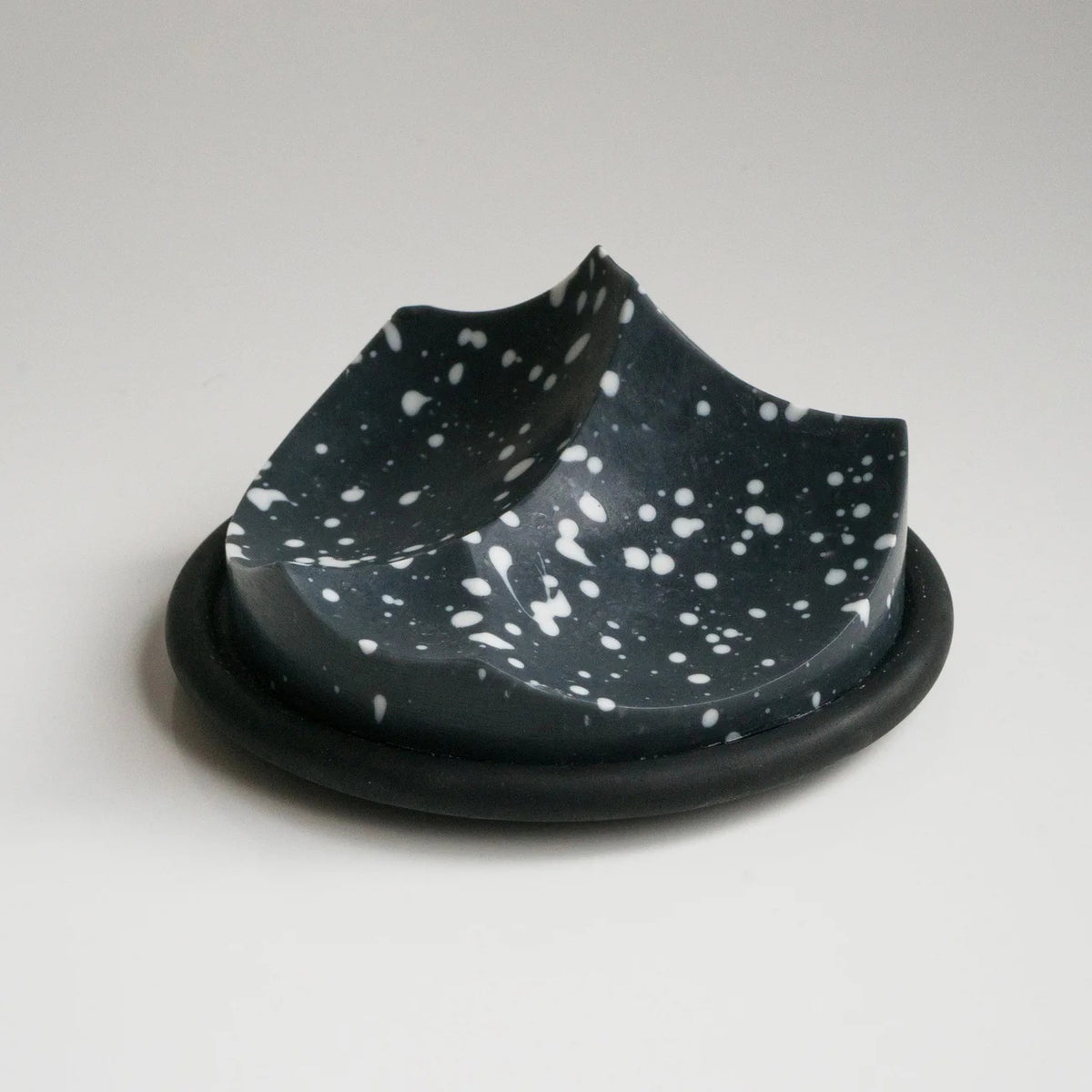 UME STUDIO’s UME - DAILY DETOX ERODE SOAP, a small round black soap with white splatter patterns, is displayed in a square white gift box with black padding. The lid and an extra box with a circular cutout sit beside it on a white surface.