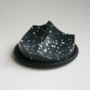 UME STUDIO’s UME - DAILY DETOX ERODE SOAP, a small round black soap with white splatter patterns, is displayed in a square white gift box with black padding. The lid and an extra box with a circular cutout sit beside it on a white surface.