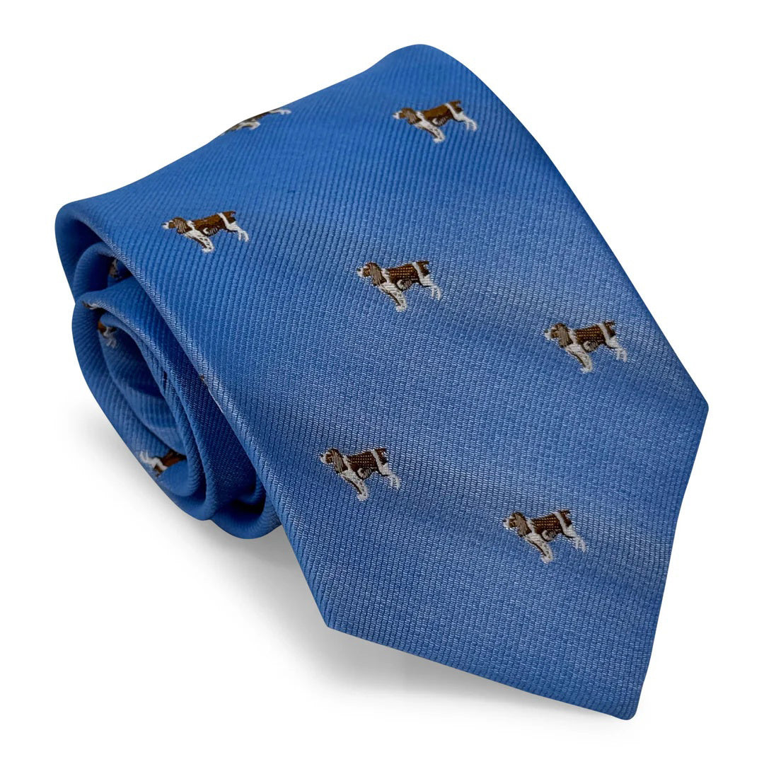 The BIRD DOG BAY - SPRINGER SPANIEL TIE by BIRD DOG BAY is a blue woven silk necktie featuring a repeating pattern of small brown and white Springer Spaniel designs.