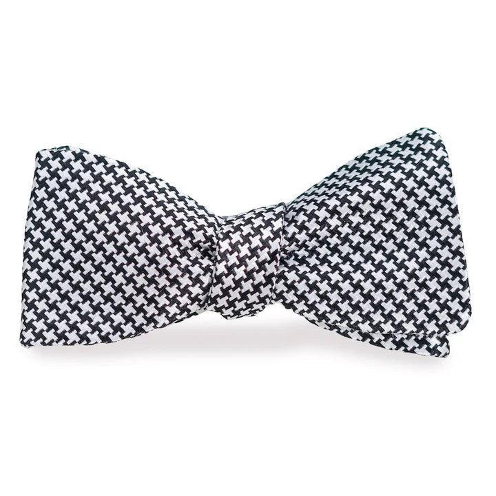 The BIRD DOG BAY - HOUNDSTOOTH SILK BOW TIE IN BLACK &amp; WHITE features a small houndstooth pattern, is handmade in the USA, and is displayed against a plain white background.