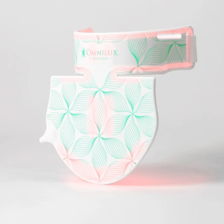 Box contents labeled: OMNILUX - CONTOUR NECK & DECOLLETE KIT by OMNILUX, featuring a flexible silicone LED device for red light therapy, rechargeable battery controller, two straps, power supply with plug adaptors, and a carry bag. The packaging is open with all items neatly arranged for your anti-aging skincare routine.